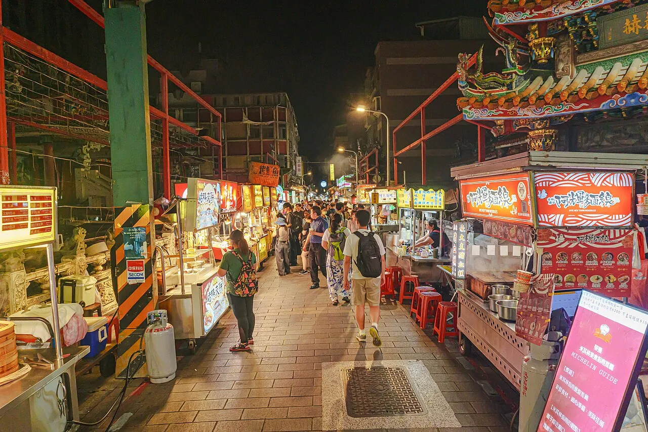 A busy night market street lined with brightly lit food stalls